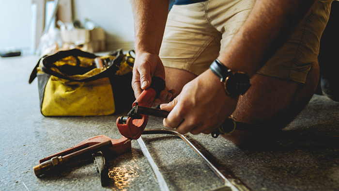 plumber on ground cutting plumbing pipes with saw