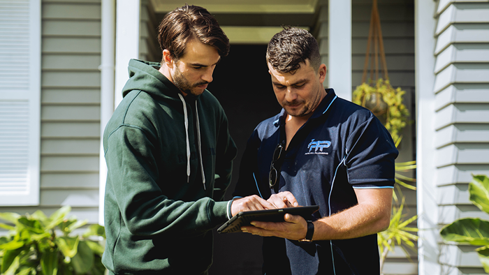 plumber and customer standing outside house looking at tablet together