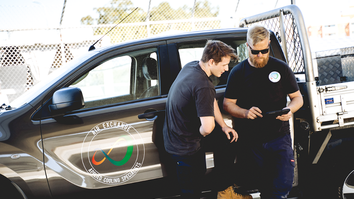 two men leaning on work van looking at device