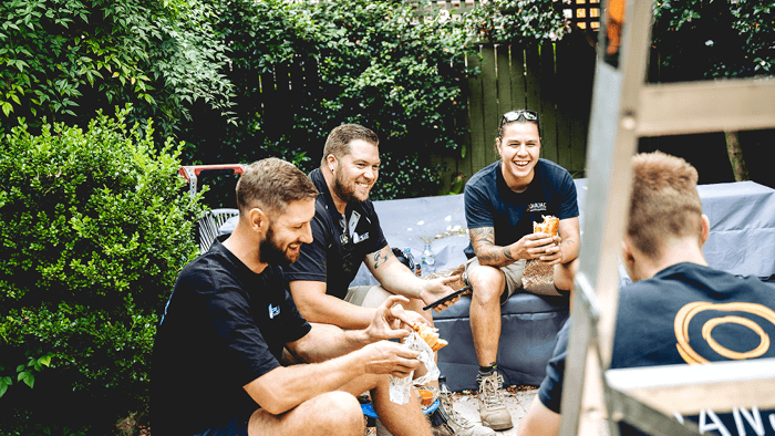 group of tradies sitting outside construction site eating lunch and laughing