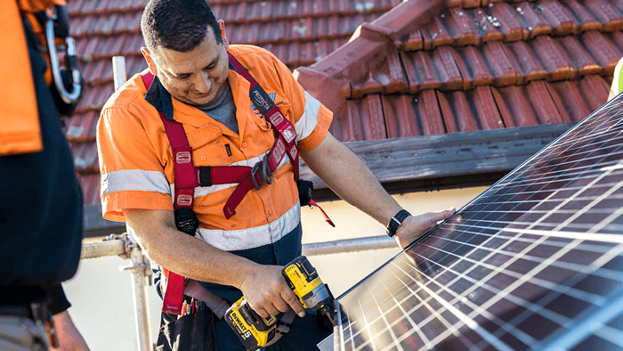 man in body harness while working on roof installing solar panels 