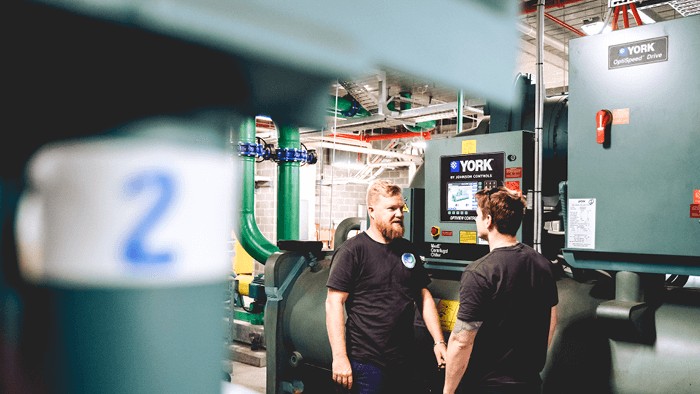 two HVAC techs standing in front of industrial heating units