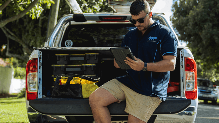 man sitting on tray of ute working on device
