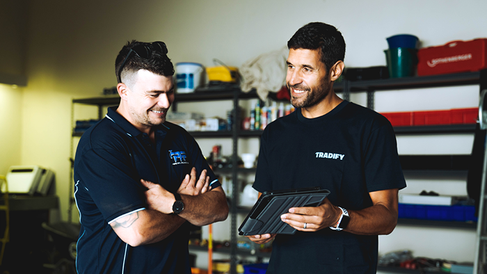 two men standing in room with shelves filled with plumbing suppliers laughing and looking at device
