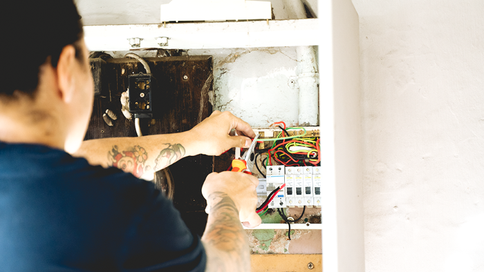 closeup of man’s back working on wiring on switch board