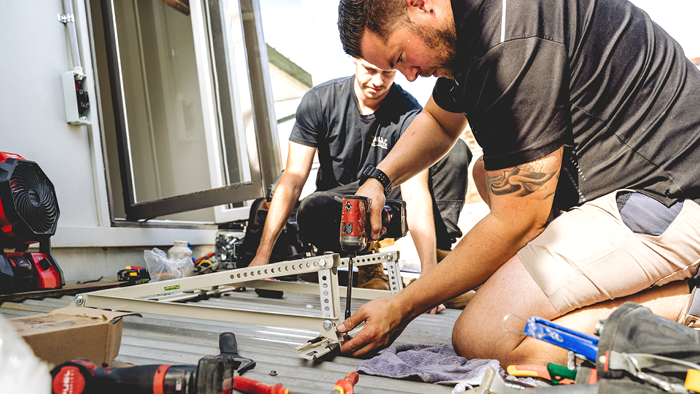 two men on roof, one making drilling screws in metal bracket