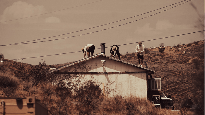 rustic photo of three tradies standing on top of a white house working on a roof with hills in the background