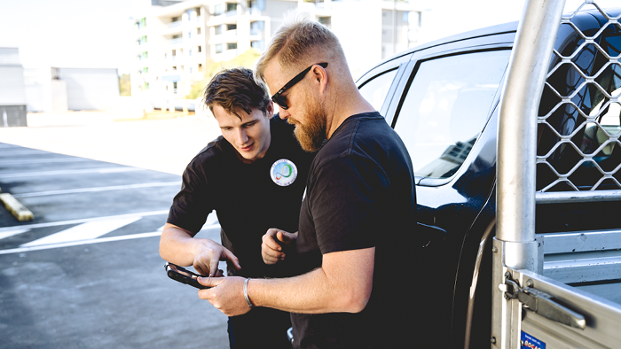 two tradies standing outside with one holding a phone and the other looking at it 