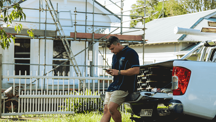 tradie sitting at the tailgate of ute looking at phone