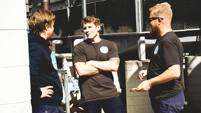 three men standing outside surrounded by metal building structure having a conversation