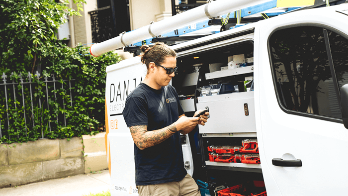 man standing outside work vehicle looking at phone 