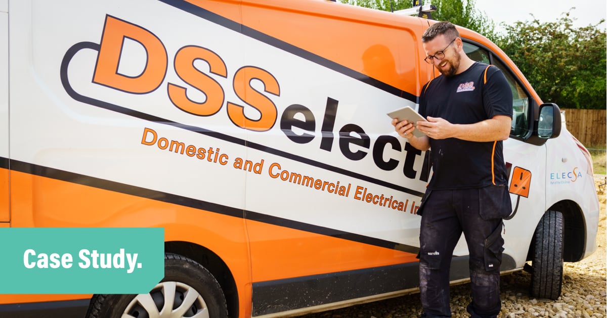 A photo of Dan standing in front of his orange van, smiling and looking at an ipad