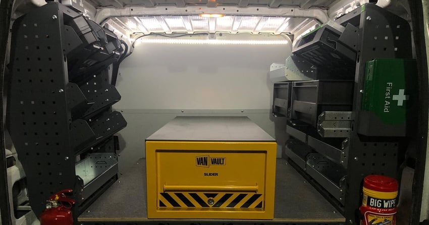 A photo showing the inside of the electrician's van lined with shelves, a yellow metal van vault, and a dark green first aid kit