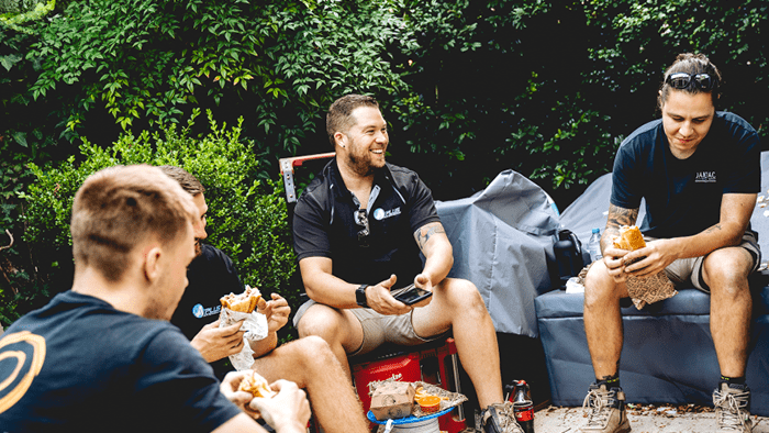 Group of tradespeople sitting down having lunch and smiling-min