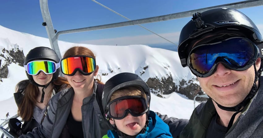 Karl with his wife, daughter and son, sitting on a ski lift travelling up a snowy mountain.