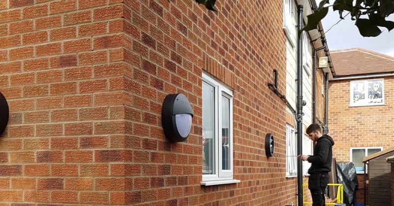 A young electrician working on an exterior light on a brown brick building