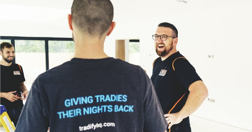 Three guys having a laugh at a job site. One wears a Tradify T-Shirt that reads "giving tradies their nights back".