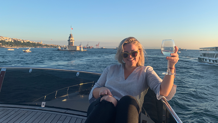 Mat_Ella_sitting at the back of a boat with a glass of wine hand and the sea behind