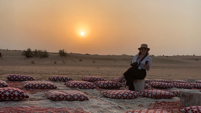 sitting on a cushion in the desert with the sun setting in the background