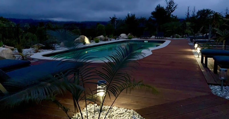 A beautiful new inground pool surrounded by decking and great lighting, lit up at night
