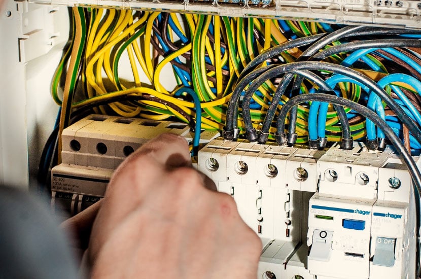 Close up of a hand working on an electrical box. There are lots of yellow, black, and blue cables