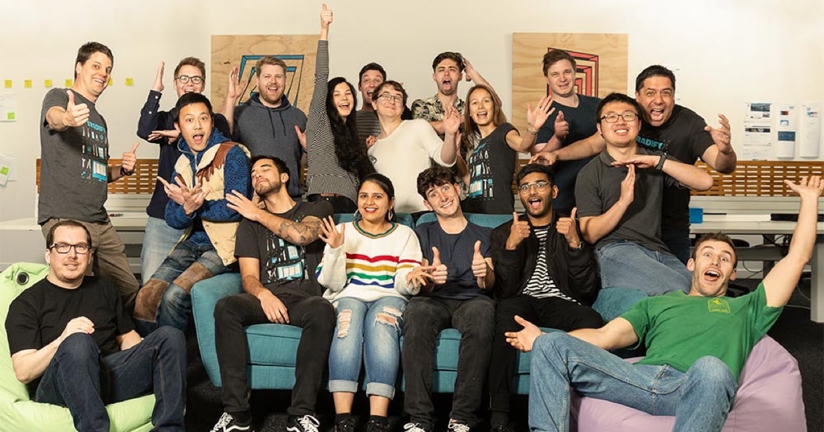 Photo of about 20 members of the Tradify team laughing and sitting around a couch