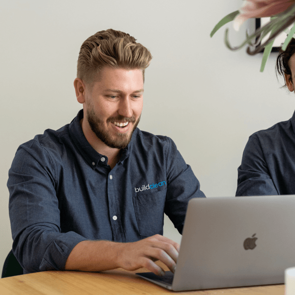 A photo of Sam Ackland, owner of Build Cleaner. He is wearing a blue shirt and working on an laptop.