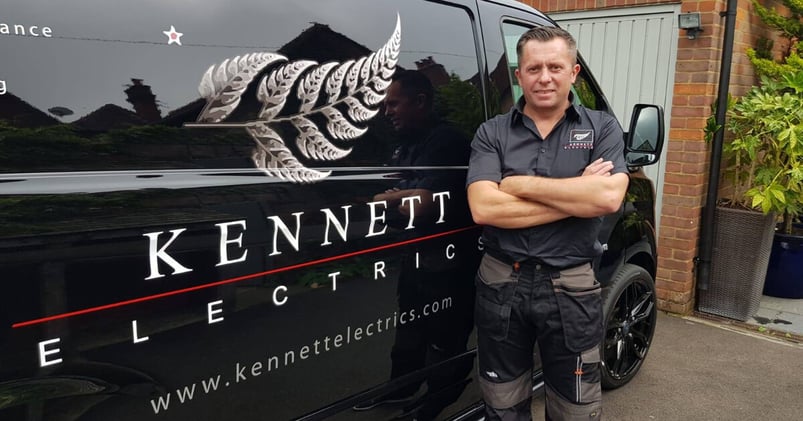 Tradify customer and electrician David Kennett stands proudly, arms folded in front of his black van sign written with his name and a silver fern