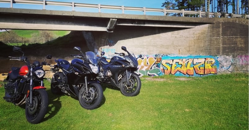 three motorbikes parked under a road bridge with graffiti in the background